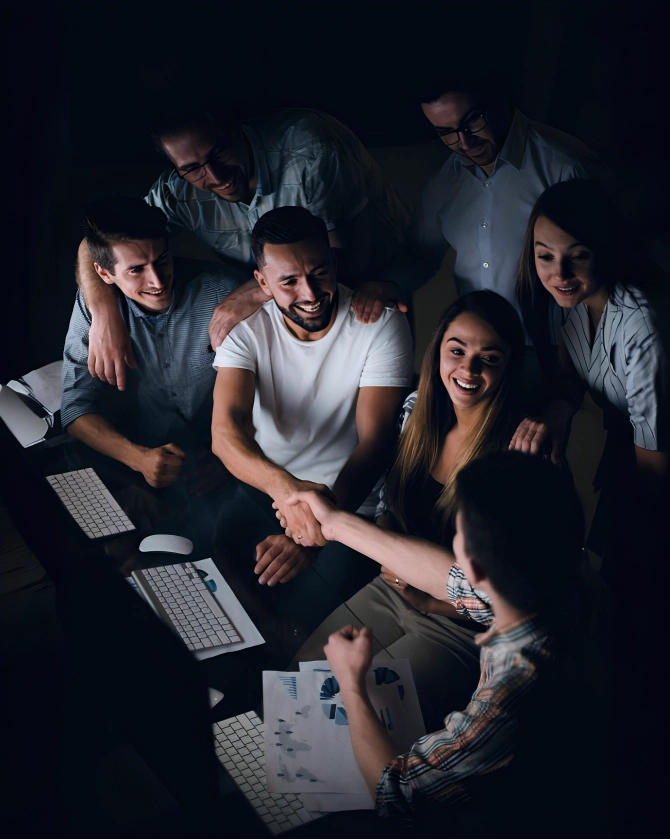 A group of smiling professionals welcoming a new team member with a handshake, symbolizing teamwork and collaboration in a creative work environment.